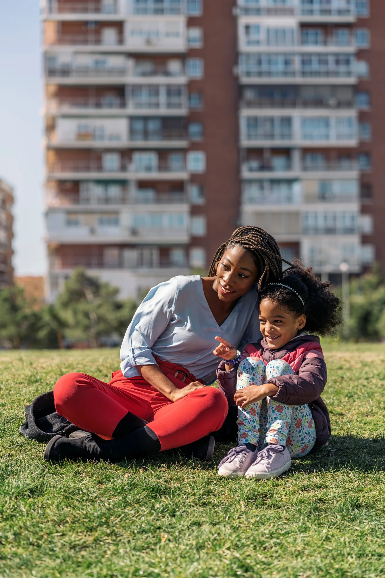 Une mère et sa fille sont assises sur un terrain gazonné devant un immeuble locatif dans le cadre de la création de l Observatoire québécois de lhabitation